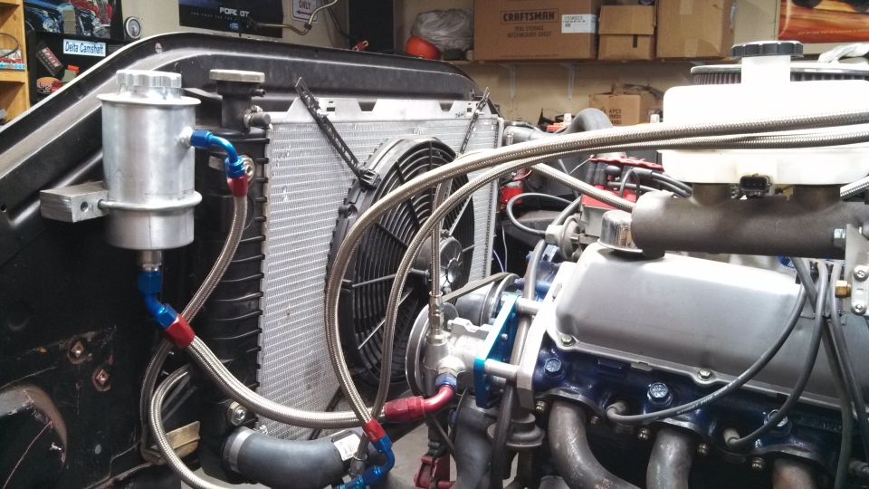 Engine bay showing radiator, electric fan, and part of a V8 engine with custom plumbing
