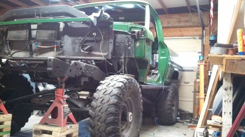 1967 Ford F-250 - A green pickup truck is in a garage, elevated on jack stands with its front end disassembled.