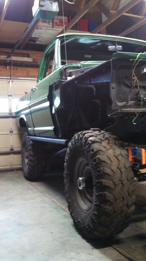 1967 Ford F-250 - A green 1967 Ford F-250 pickup truck is partially disassembled in a garage, showing its large tires and lifted suspension.