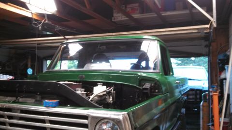 1967 Ford F-250 - A green pickup truck is parked inside a garage with its hood open, revealing the engine compartment.
