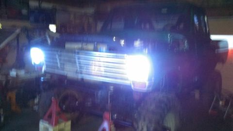 1967 Ford F-250 - Front view of a 1967 Ford F-250 truck with its headlights illuminated, appearing to be undergoing maintenance.