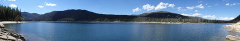1994 Ford Bronco - A vast expanse of water is bordered by trees and hills under a bright, cloud-dotted sky.