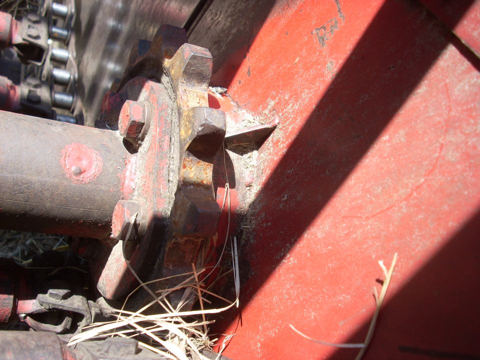 Close-up of a rusty metal gear and chain on a red agricultural machine