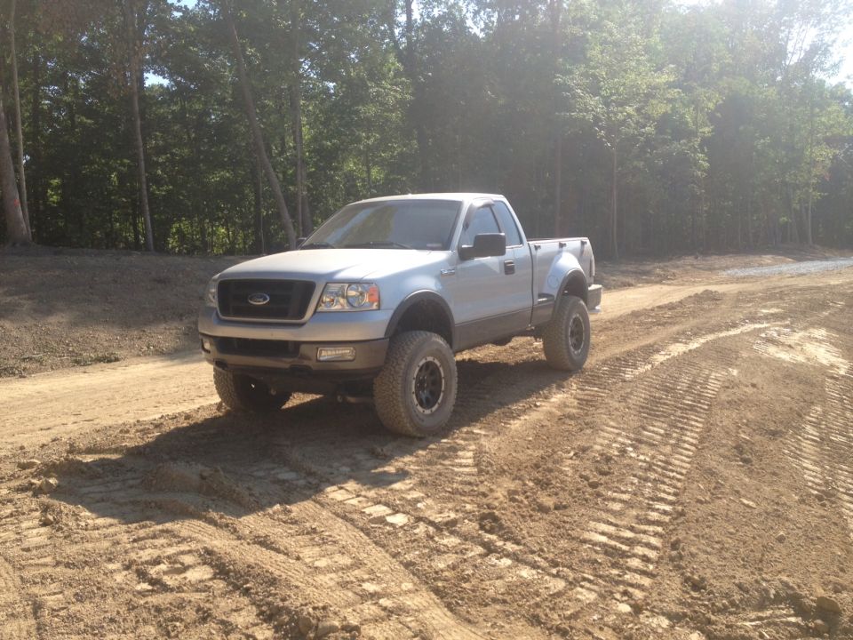 Silver Ford F-150 pickup truck, lifted with off-road tires, driving on a dirt track
