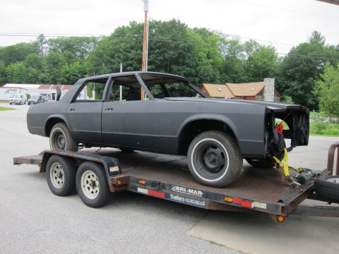1991 Ford LTD Crown Victoria - A matte gray sedan, likely a project car, is transported on a trailer, missing its front grille and hood.