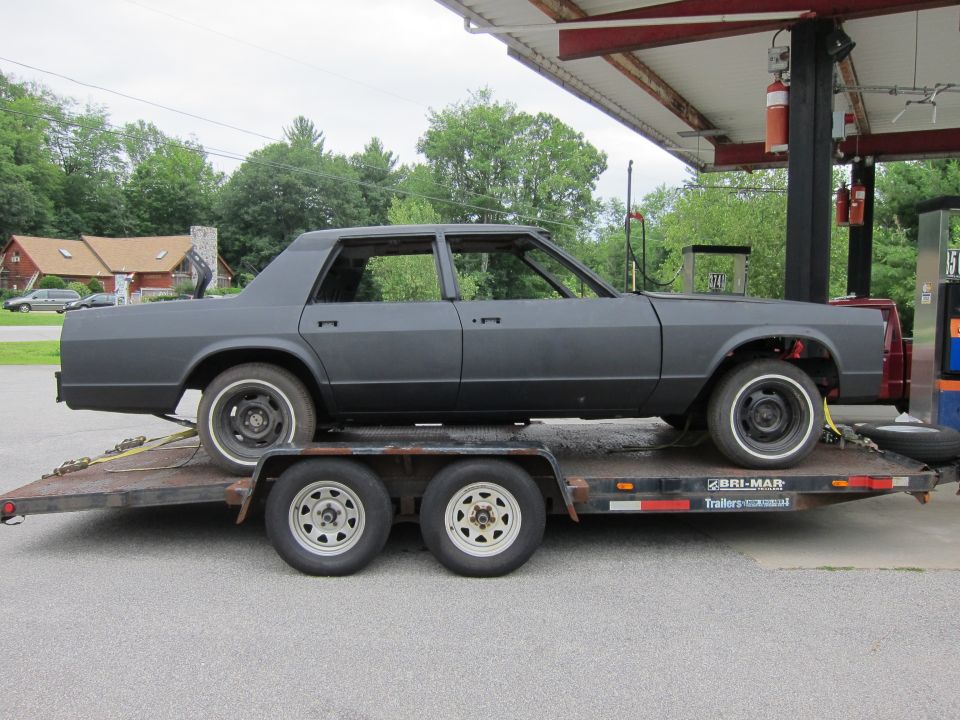 Gray sedan body on a trailer at a gas station, missing windows and doors