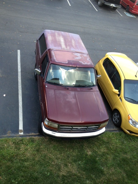 1996 Ford Bronco - A maroon 1996 Ford Bronco is parked in a lot next to a yellow compact car.