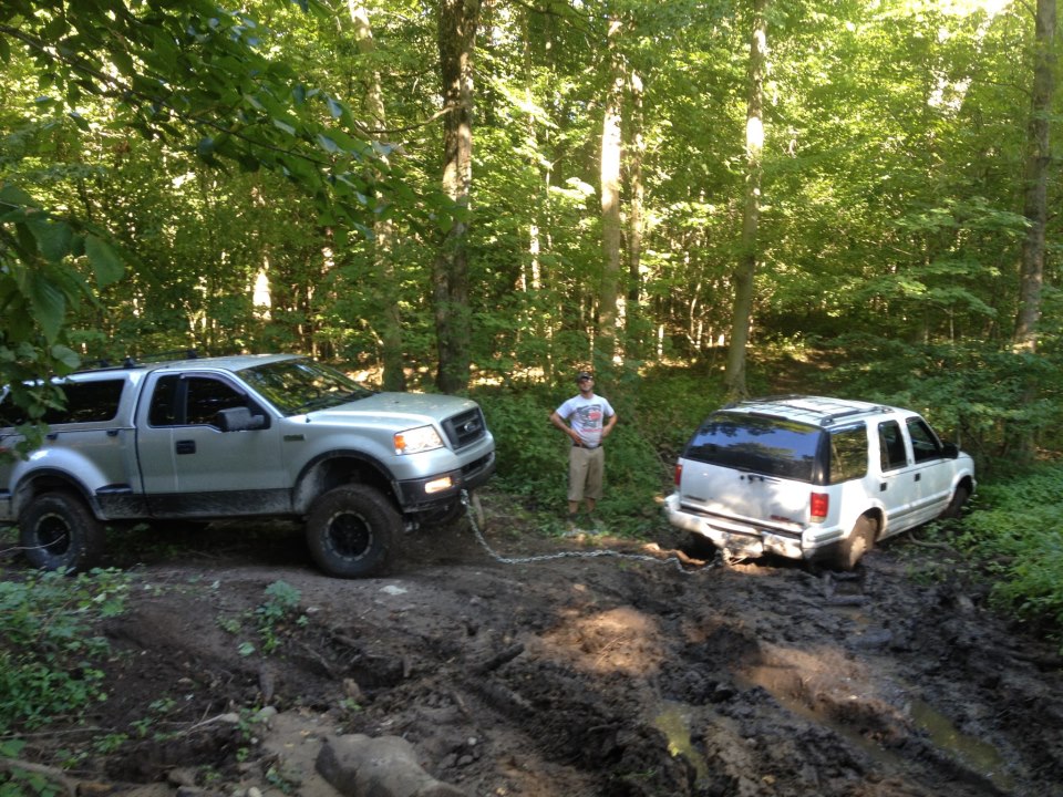 Silver Ford F-150 pulling a white SUV out of mud in a forest
