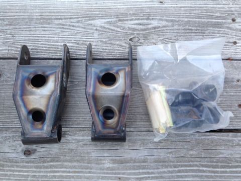 1986 Ford Bronco - Aftermarket suspension shackles and hardware are laid out on a wooden surface.