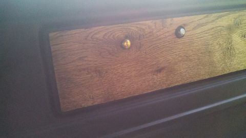 1979 Ford Bronco - Close-up of a wood-grain trim panel with two fasteners, possibly from a vehicle interior.