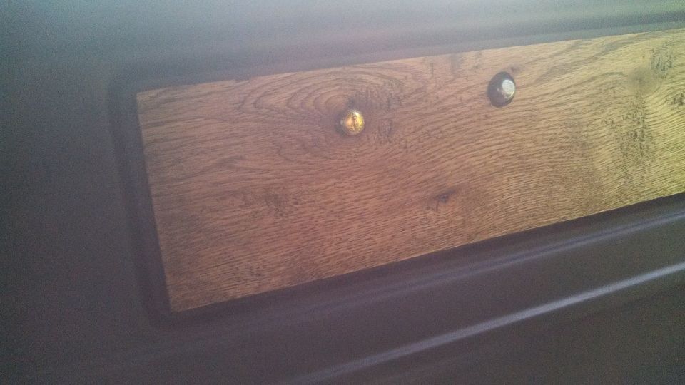 Wood trim panel with brass and silver fasteners on dark interior surface