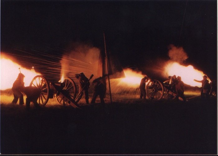 Cannons firing at night with sparks and smoke, men operating them