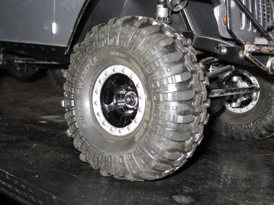 Close-up of a large, knobby tire on an RC rock crawler. The tire is labeled 'SUPER SWAMPER'