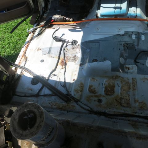 1995 Ford Bronco - The interior of a vehicle is shown stripped down, revealing rust and exposed wiring, with tools nearby.
