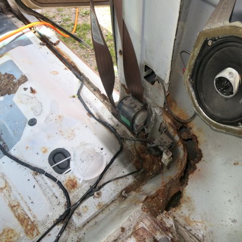 1995 Ford Bronco - The interior of the vehicle shows extensive rust damage, particularly around the floor and seatbelt anchor points.