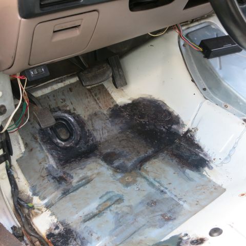 1995 Ford Bronco - The interior floor of a vehicle shows exposed metal and patches of sealant, with wiring visible near the pedals.