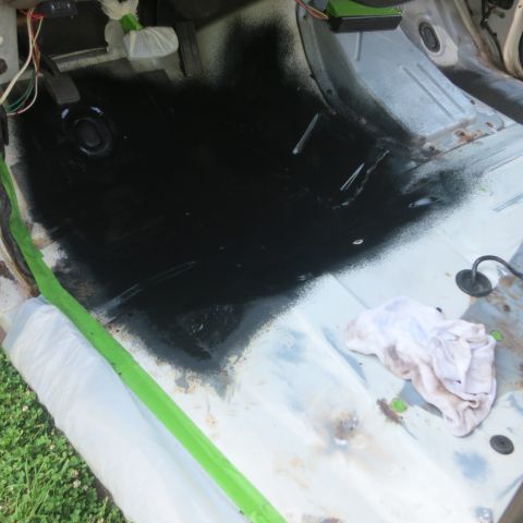 1995 Ford Bronco - The interior floor of a vehicle is being sprayed with black paint, with protective coverings in place.