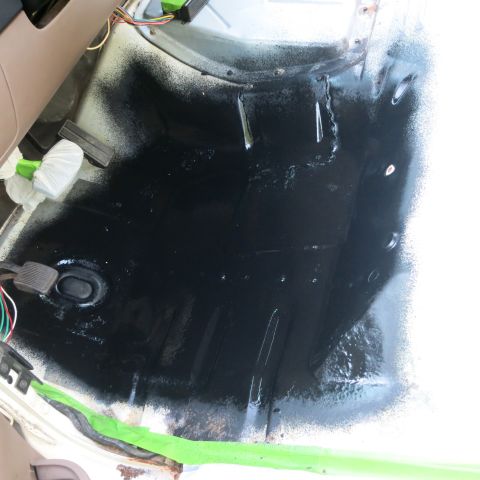 1995 Ford Bronco - The interior floor pan of a vehicle is coated in black, with pedals and wiring visible.