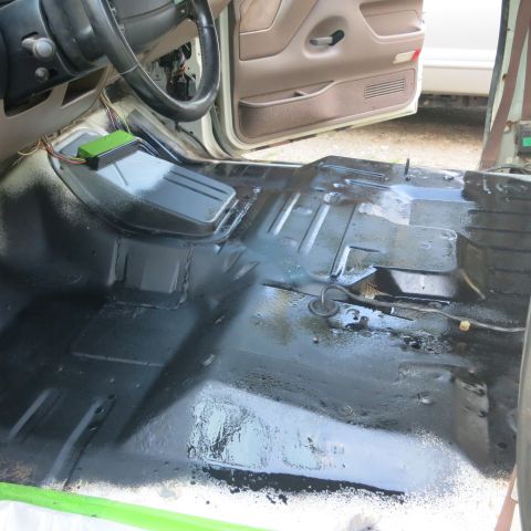 1995 Ford Bronco - The interior floor of a vehicle is coated in black, with the steering wheel and door visible.