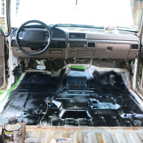 1995 Ford Bronco - The interior of a vehicle is shown with the floor stripped and coated in black undercoating, ready for further work.