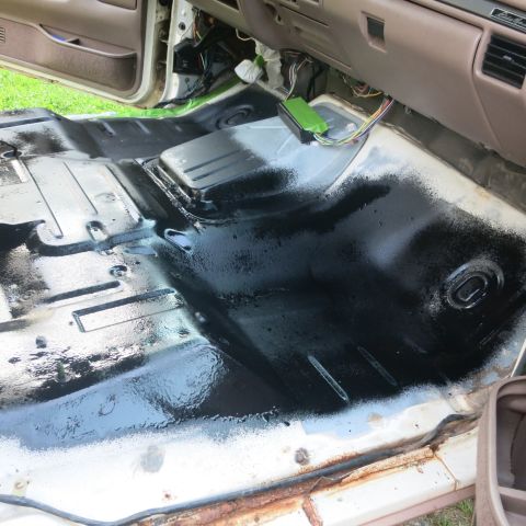 1995 Ford Bronco - The interior floor of a vehicle is being painted black, showing exposed wires and a green electrical box.