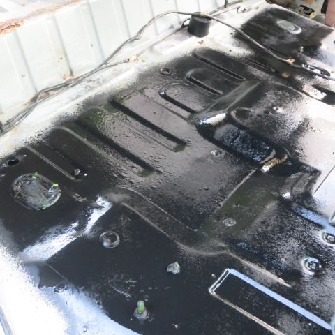 1995 Ford Bronco - The undercarriage of a vehicle has been coated with a black protective substance, showing structural ribs and mounting points.