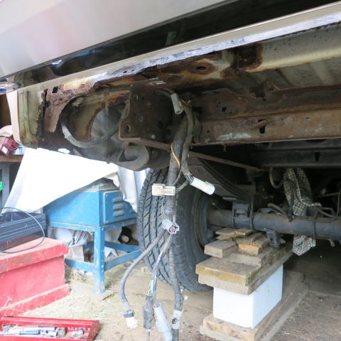 1995 Ford Bronco - The rear underside of a vehicle shows extensive rust damage and exposed wiring.
