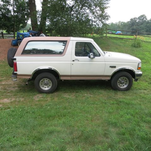 1995 Ford Bronco - A white 1995 Ford Bronco with a tan removable top is parked on a grassy lawn, a spare tire mounted on the rear tailgate.
