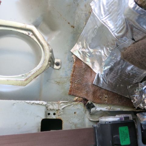 1995 Ford Bronco - The interior of a vehicle shows exposed metal, insulation material, and a seatbelt anchor point.