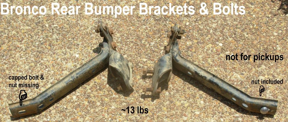 Pair of rusty Ford Bronco rear bumper brackets with bolts on gravel, with labeled text