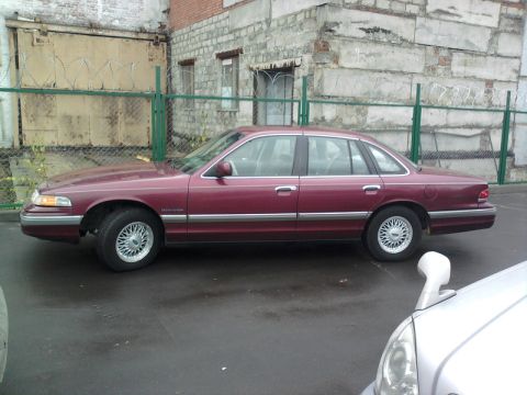 1992 Ford Crown Victoria - Maroon 1992 Ford Crown Victoria parked next to a building with a chain-link fence.