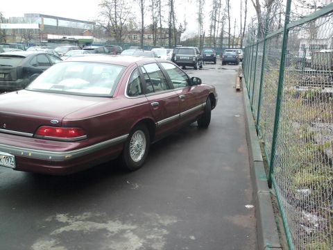 1992 Ford Crown Victoria - A maroon 1992 Ford Crown Victoria is parked next to a chain-link fence.