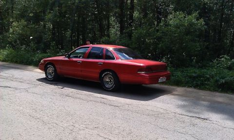 1992 Ford Crown Victoria - A red 1992 Ford Crown Victoria is parked on the side of a road with trees in the background.
