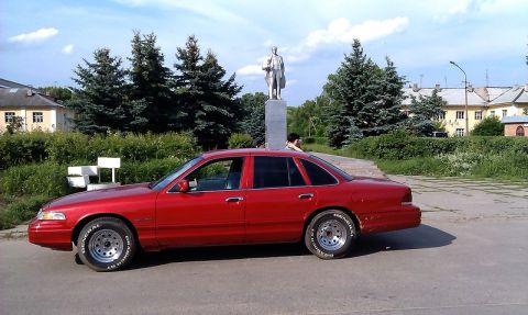 1992 Ford Crown Victoria - A red 1992 Ford Crown Victoria sedan is parked outdoors near a statue and trees.