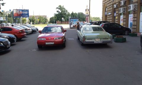 1992 Ford Crown Victoria - Two sedans, a red Ford and a light green Cadillac, are parked on a city street.