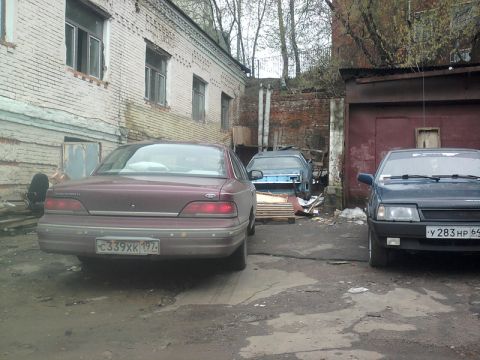 1992 Ford Crown Victoria - A maroon sedan is parked in an alley next to other vehicles and a brick building.