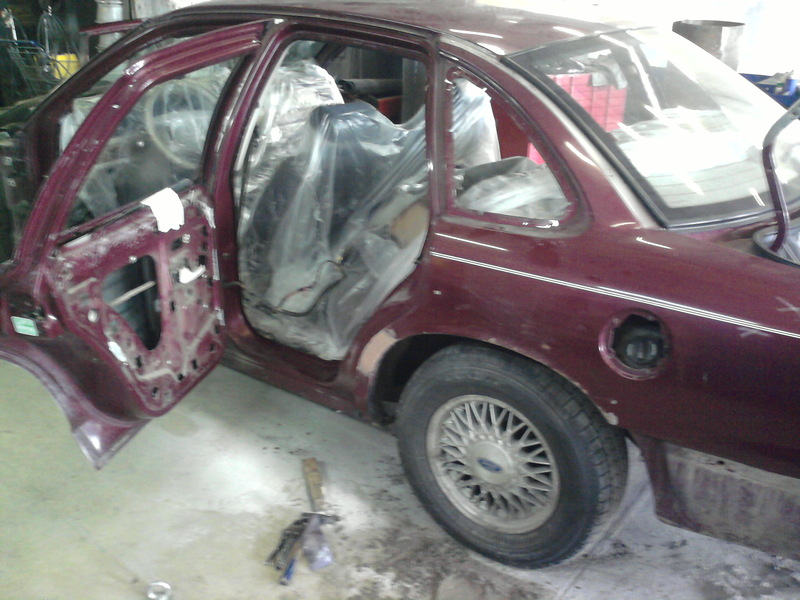 Maroon sedan with doors open and interior covered in plastic, parked inside