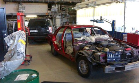 1992 Ford Crown Victoria - A red sedan is in a repair shop with its doors open and engine compartment exposed, while a black SUV is parked behind it.