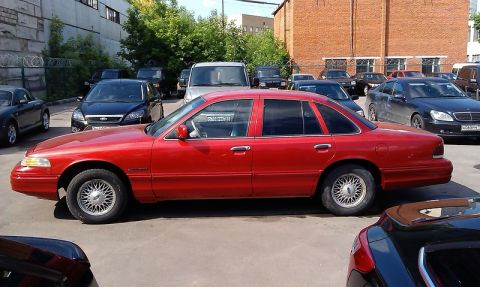 1992 Ford Crown Victoria - A red 1992 Ford Crown Victoria sedan is parked in a lot with other vehicles.