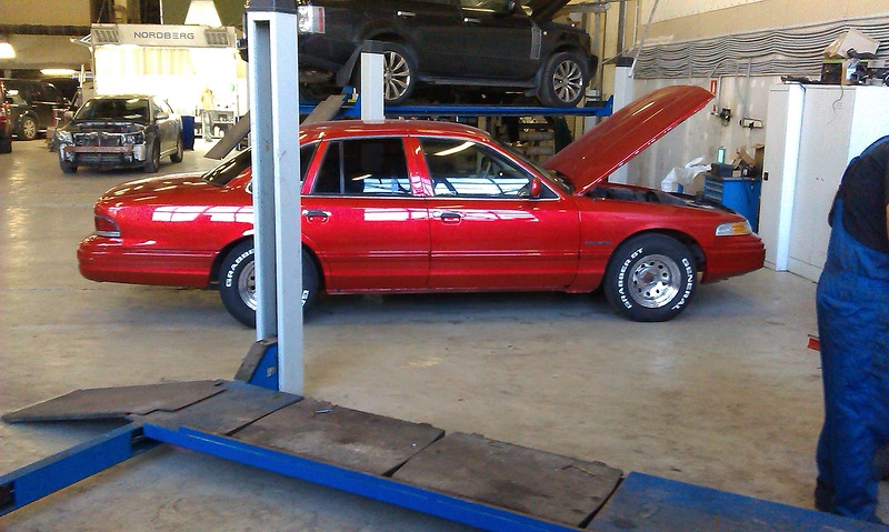 Red 1992 Ford Crown Victoria sedan with hood open, on a car lift, side view