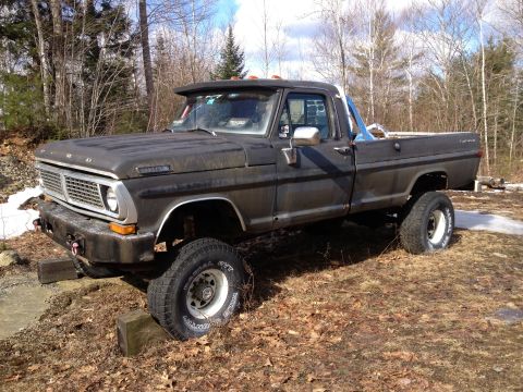 1979 Ford Bronco - This lifted Ford truck is parked on uneven ground with trees in the background.