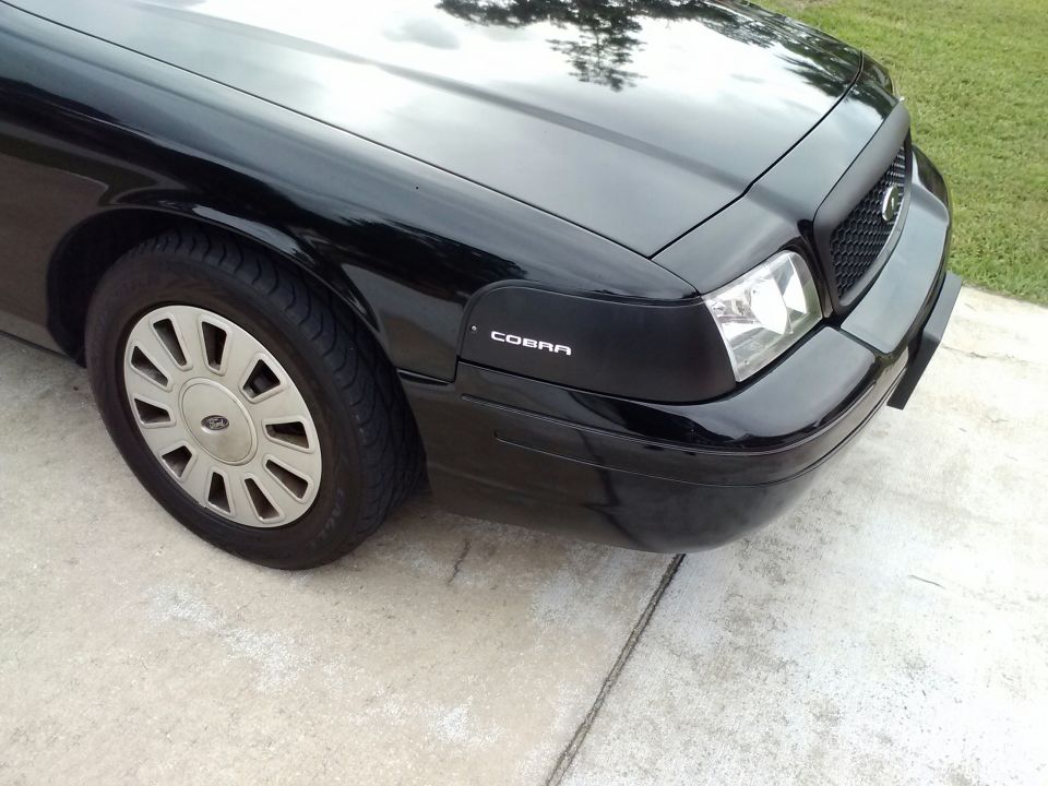 Black Ford Crown Victoria front fender with "COBRA" badge, silver hubcap, and headlight
