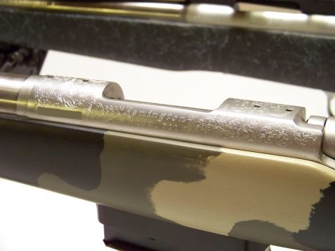 1995 Mercury Grand Marquis - Close-up of an engraved rifle receiver with a camouflage stock and a portion of another rifle visible in the background.