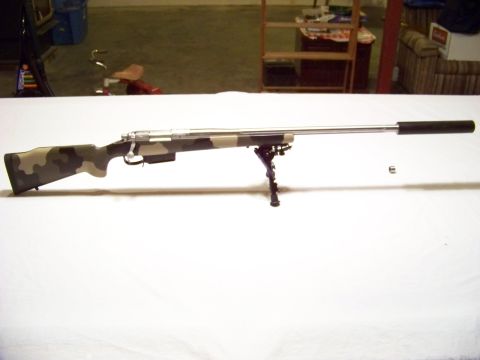 1995 Mercury Grand Marquis - A camouflage sniper rifle rests on a table, equipped with a bipod and suppressor.