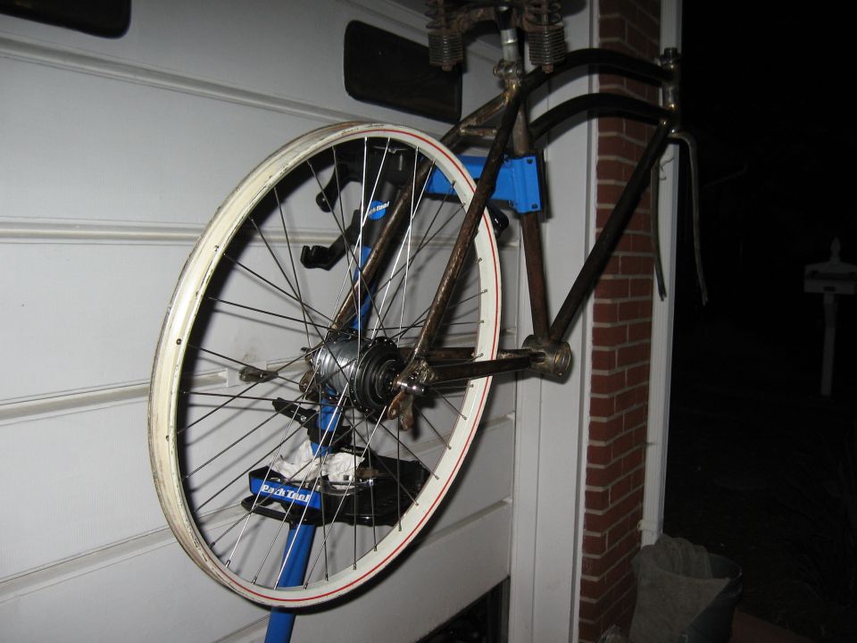 Bicycle frame and wheel mounted on a blue stand against a white wall
