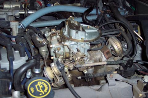 1991 Ford LTD Crown Victoria - Engine bay detail showing a carburetor and associated hoses and wiring. The oil cap is visible.