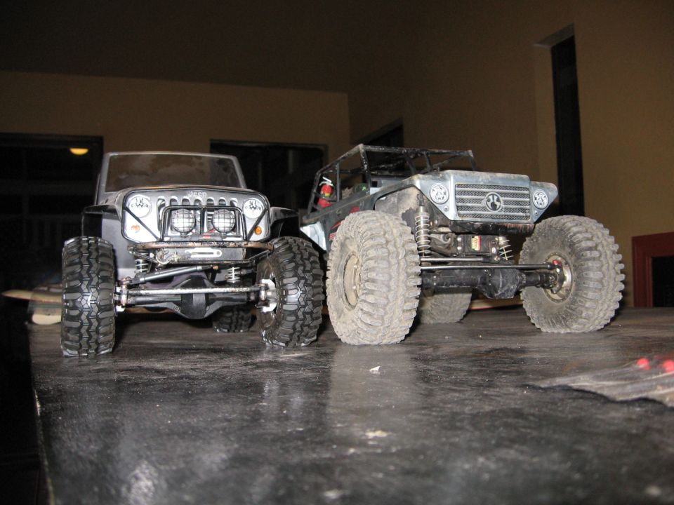 Two RC rock crawler trucks with large tires and custom bodies are parked on a table