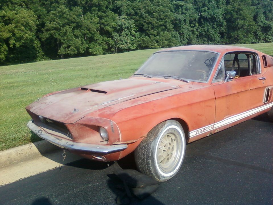 Orange 1967 Ford Mustang GT350 with white racing stripes, dusty and weathered, parked on asphalt