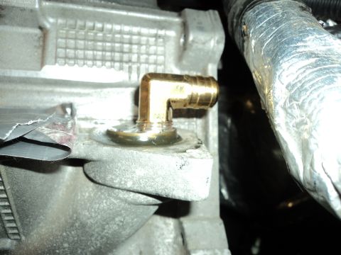2004 Mercury Grand Marquis - A brass elbow fitting is installed on a textured metal engine part, with a silver insulated hose visible to the right.