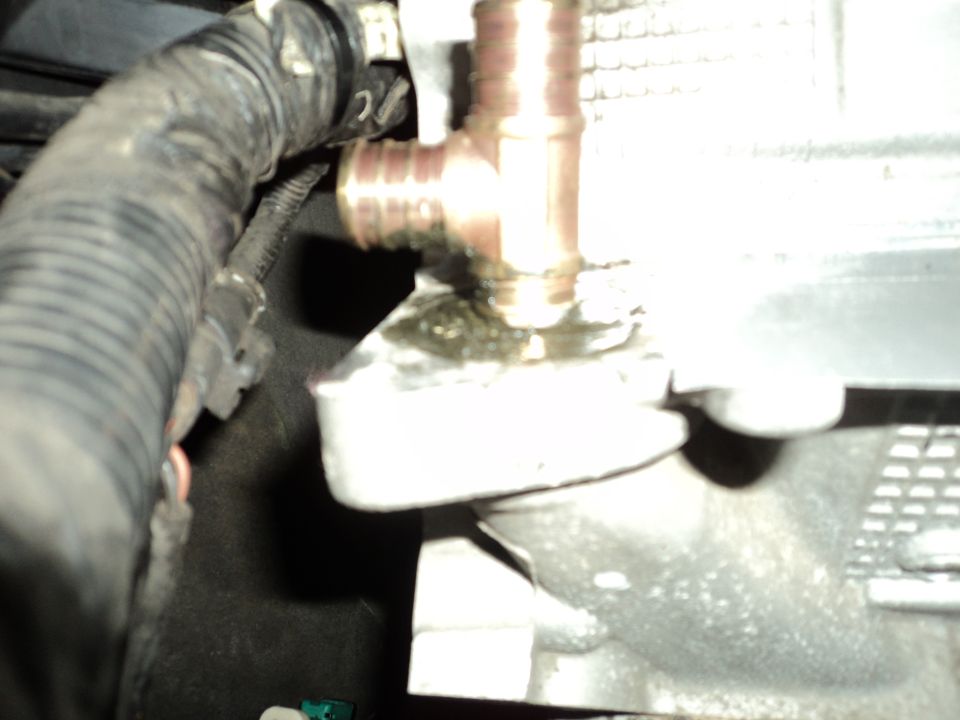 Close-up of a brass T-fitting connected to a ribbed hose, with some fluid leakage